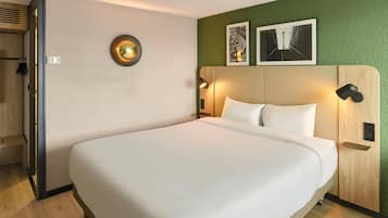 A hotel room with a large bed, a wooden headboard, two wall-mounted lights, and two framed pictures on the wall.