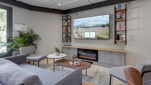Una sala de estar moderna con un televisor de pantalla plana, chimenea, sofás grises, una mesa de centro y una estantería.