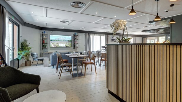 A modern dining area with a large window, a wooden partition, and a variety of seating options including a sofa and chairs.