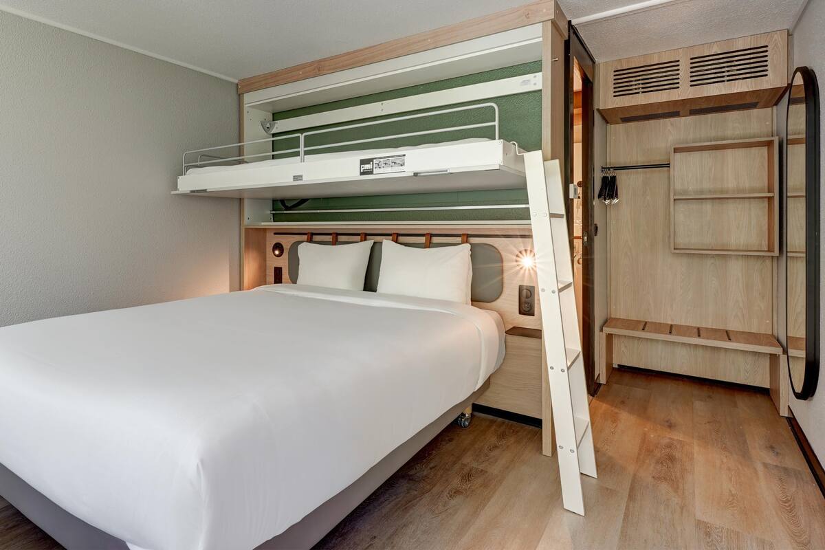 A bunk bed with a lower bunk, a wooden headboard, and a bedside table with a lamp.