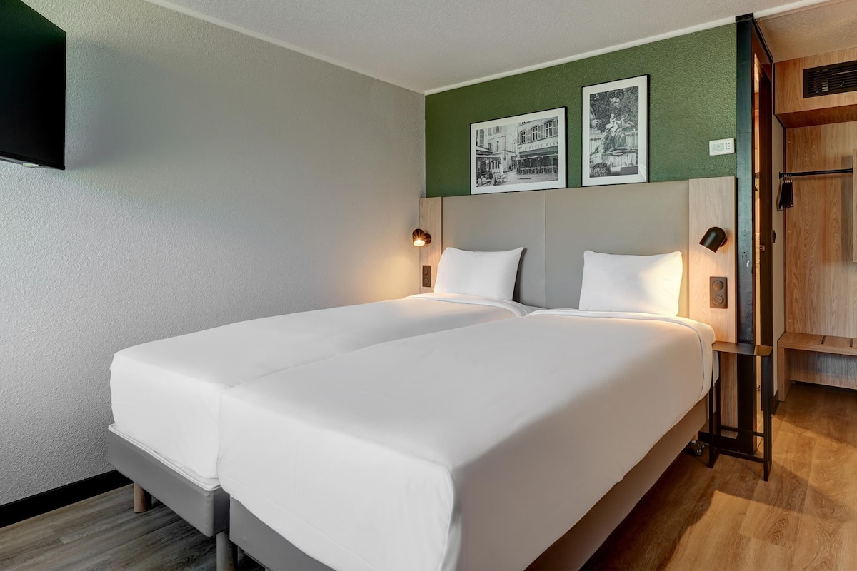 A double bed with white linens, a wall-mounted TV, and two framed pictures above it.