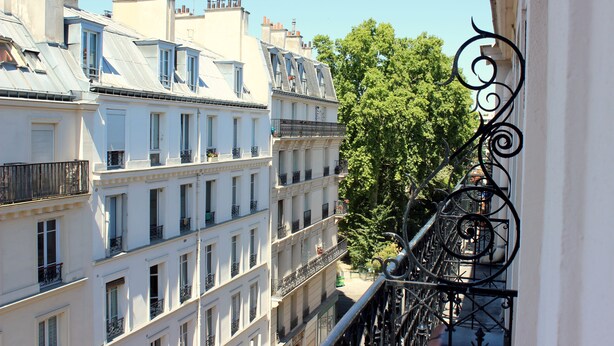 A view of multi-story buildings with balconies and a tree in the background.
