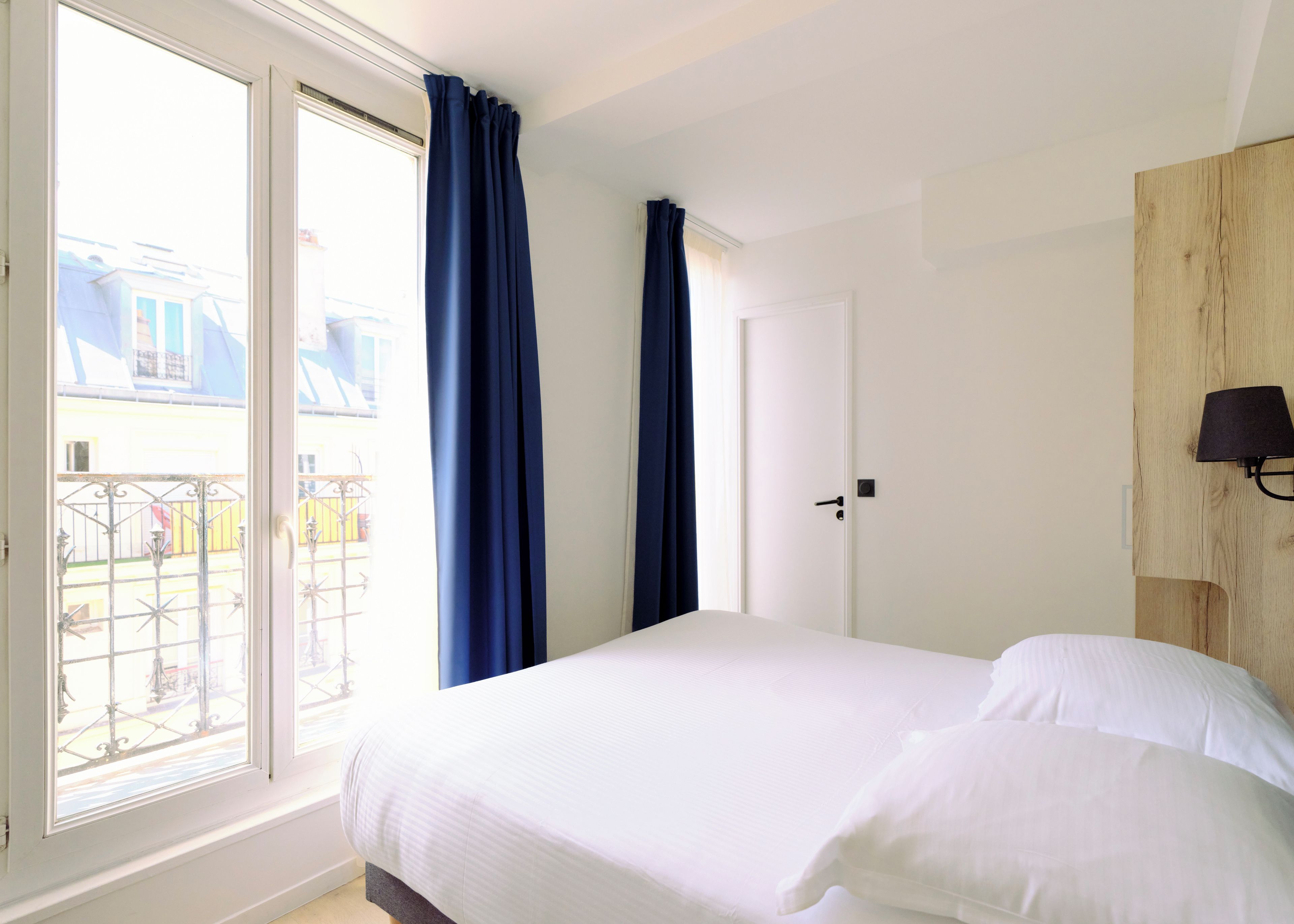 A hotel room with a bed, a door, and a window with curtains.