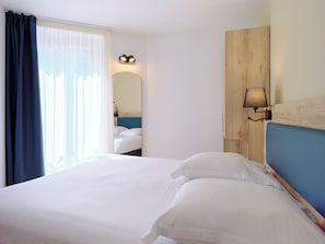 A hotel room with a bed, a mirror, and a wall-mounted lamp. - Hotel du Chemin Vert Paris (Paris)