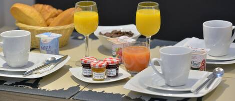 A breakfast table with croissants, orange juice, coffee, and jam.