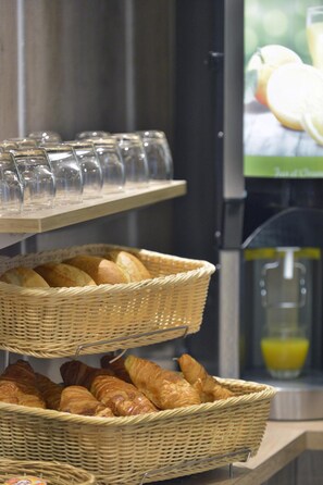 A breakfast buffet with wicker baskets of bread and croissants, and a glass display case with clear glasses. - Hotel du Chemin Vert Paris (Paris)