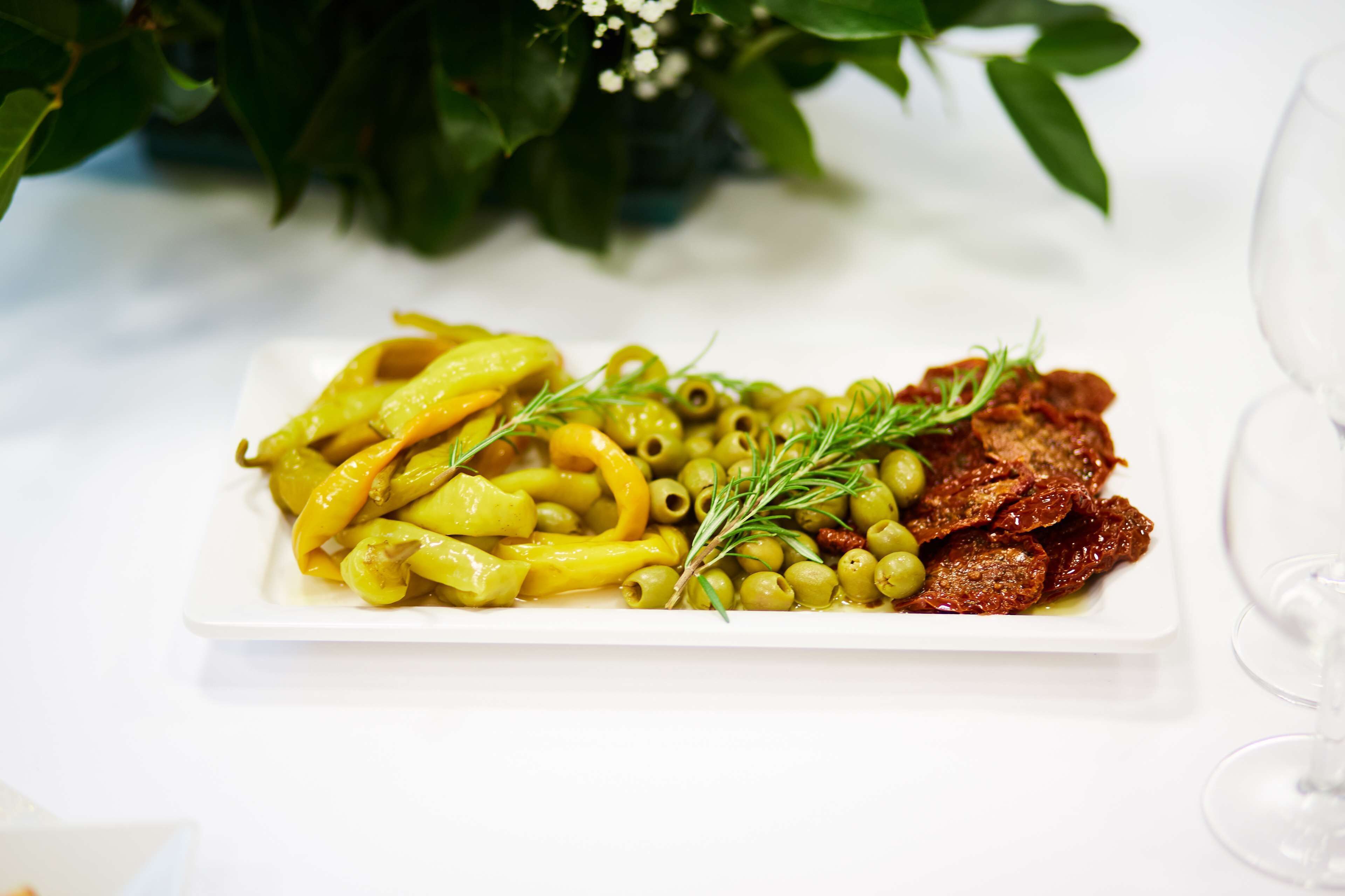 Ein weißer Teller mit gelben Paprika, grünen Oliven und Rosmarinzweigen.