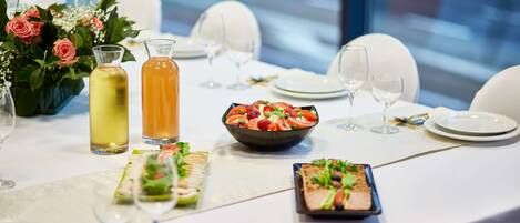 Mesa dispuesta para una comida, con un centro de mesa floral, ensalada en un tazón y una botella de bebida.