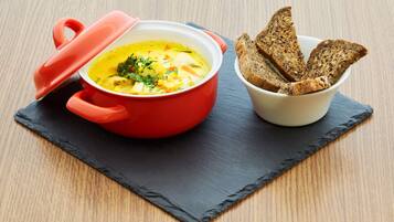 Une casserole rouge avec un couvercle, posée sur une planche d’ardoise noire, à côté d’un bol de tranches de pain.