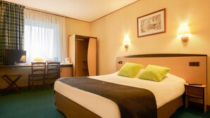 Habitación de hotel con una cama, dos sillones, un escritorio, un televisor y dos lámparas de pared.