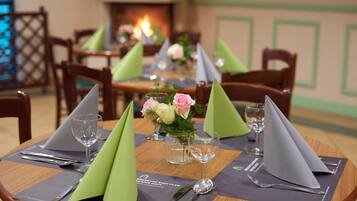 A dining table set with green napkins, silverware, and a vase with flowers.