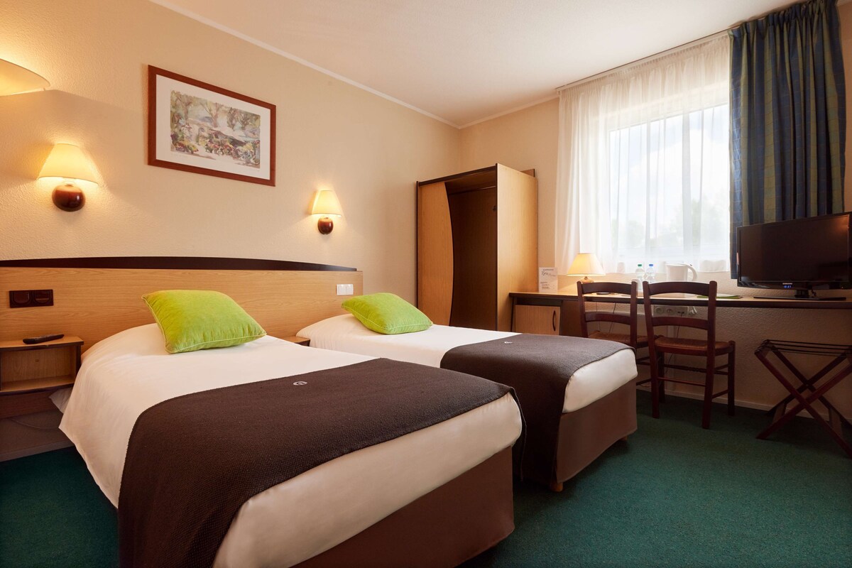 A hotel room with two beds, a desk, a television, and a window with curtains.
