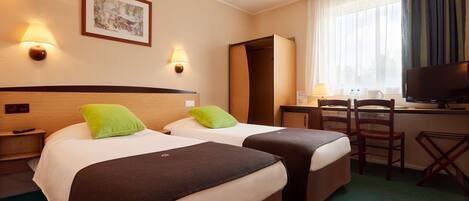 A hotel room with two beds, a desk, a television, and a window with curtains.