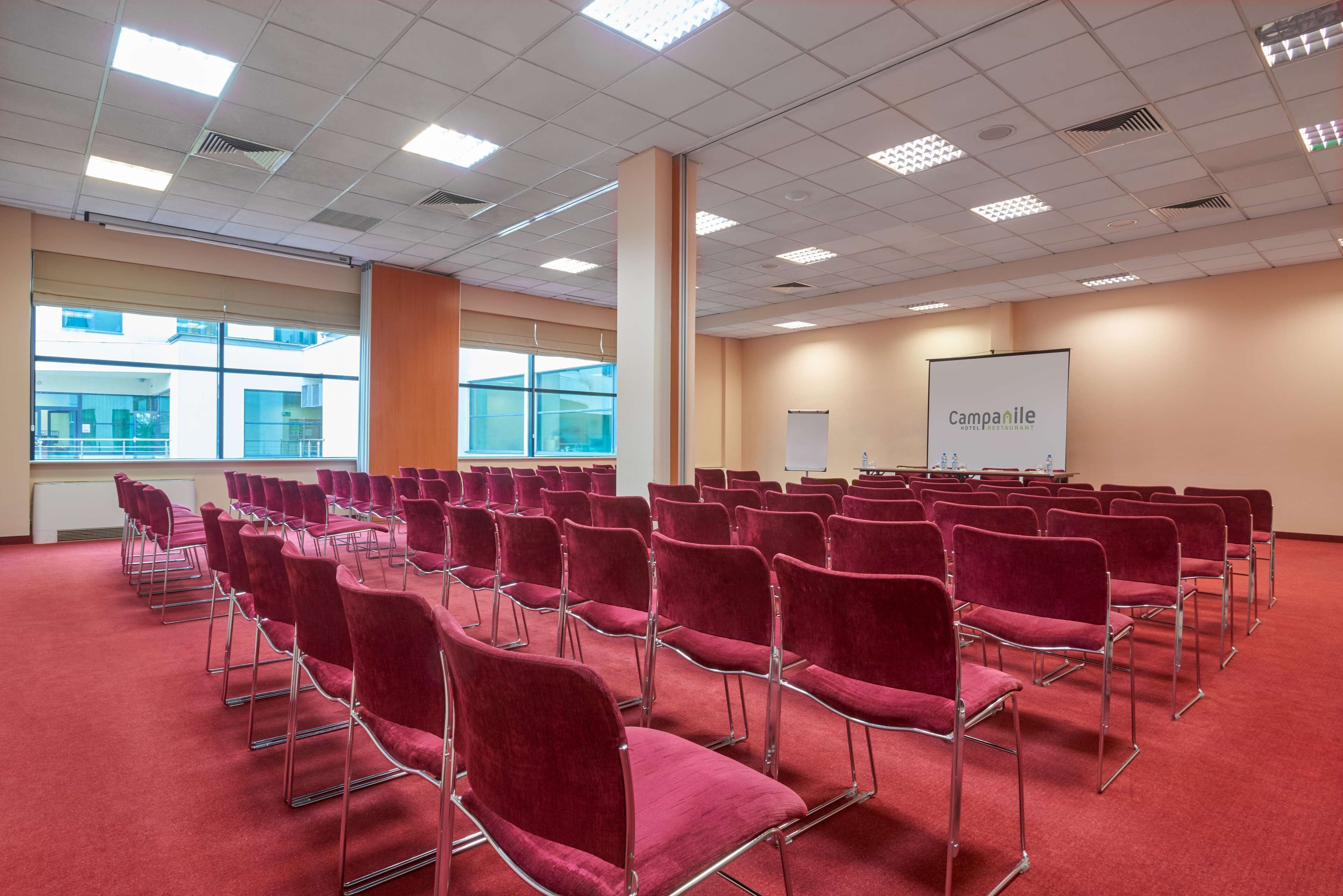 A conference room with rows of red chairs, a whiteboard, and a projector screen displaying "campanile."