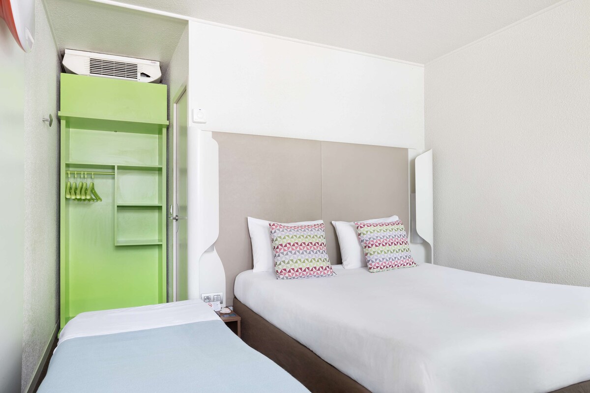 A hotel room with a green wardrobe, a bed with patterned pillows, and a white headboard.