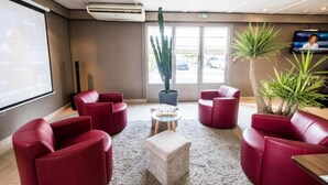 Un vestíbulo con sofás de cuero rojo, una pequeña mesa redonda, un cactus en maceta y un televisor en la pared.