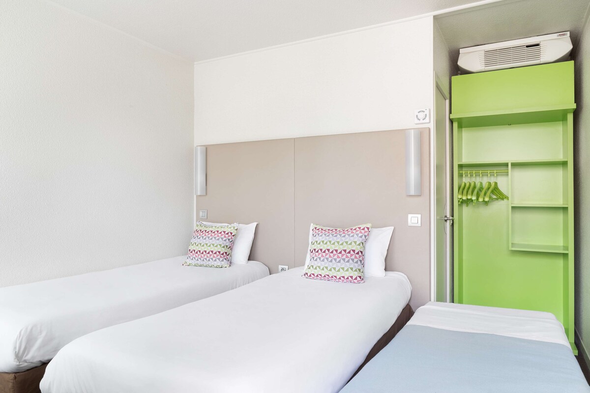 A hotel room with two beds, a green wardrobe, and a ceiling-mounted air conditioner.