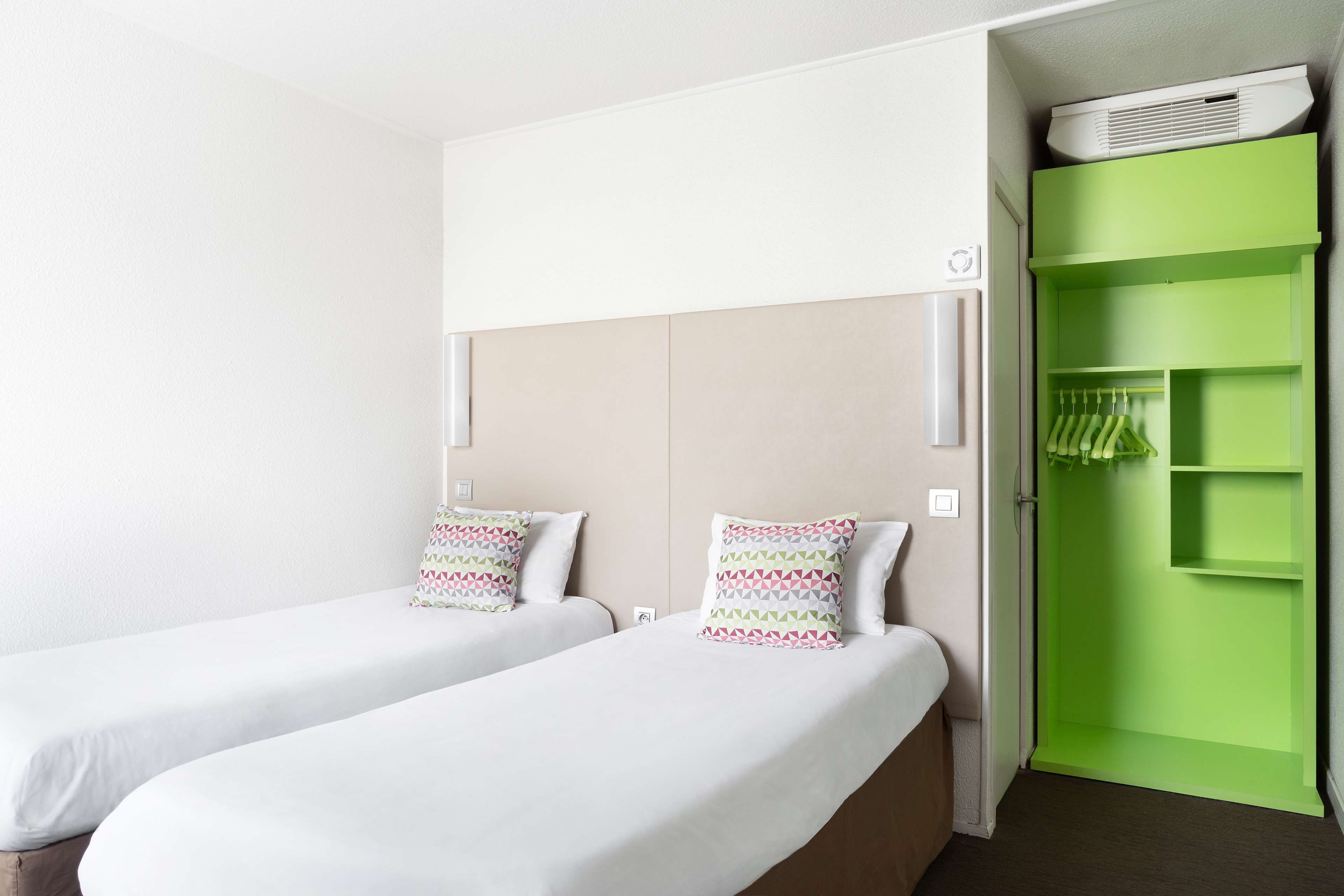 Habitación de hotel con dos camas individuales, un armario verde y un equipo de aire acondicionado blanco.