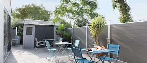 Un patio al aire libre con sillas plegables azules y una mesa, rodeado por una cerca gris y árboles.