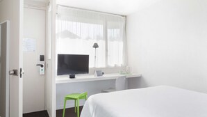 Habitación de hotel con cama, escritorio con computadora, silla y ventana con cortinas.