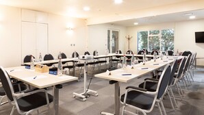 Un salón de conferencias con mesas largas, sillas, tarjetas de identificación, botellas de agua y un proyector.