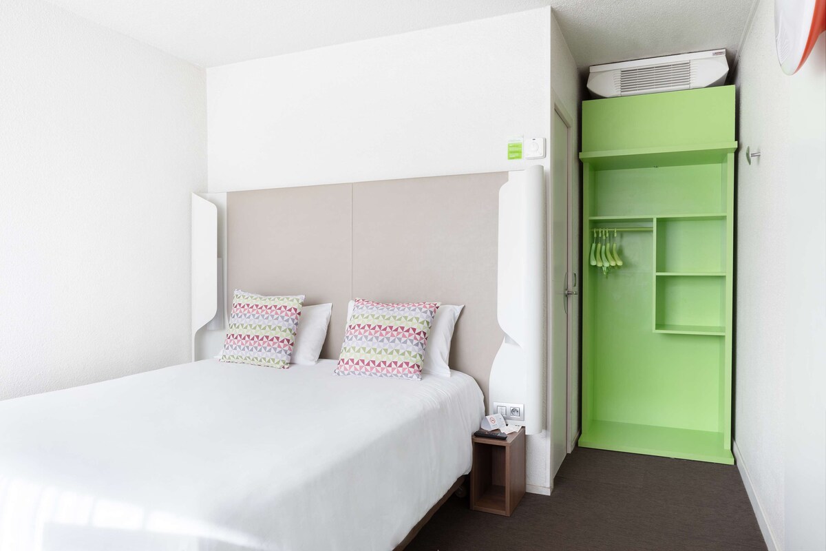 A hotel room with a bed, a green wardrobe, and a small bedside table.