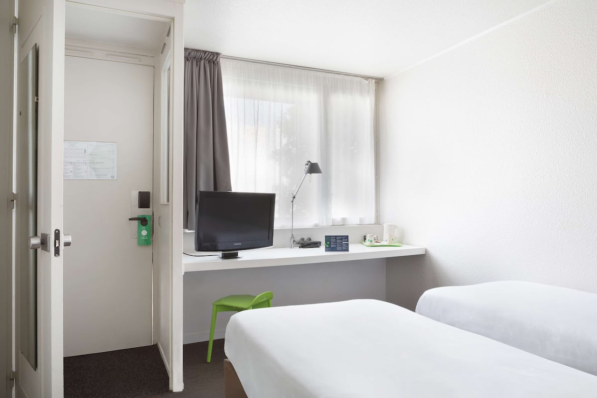 Habitación de hotel con escritorio, televisión, una silla verde y dos camas.