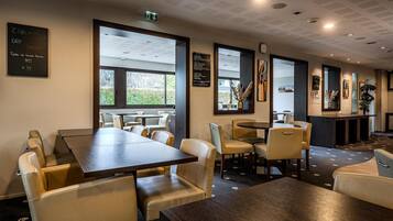 Um restaurante com decoração moderna, apresentando uma combinação de móveis de madeira escura e clara, grandes janelas que permitem entrada de luz natural, e um cardápio em uma lousa na parede.