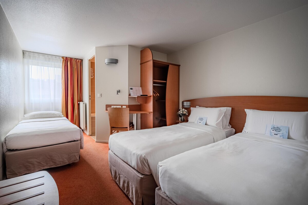 A hotel room with two beds, a desk, a chair, and a closet.