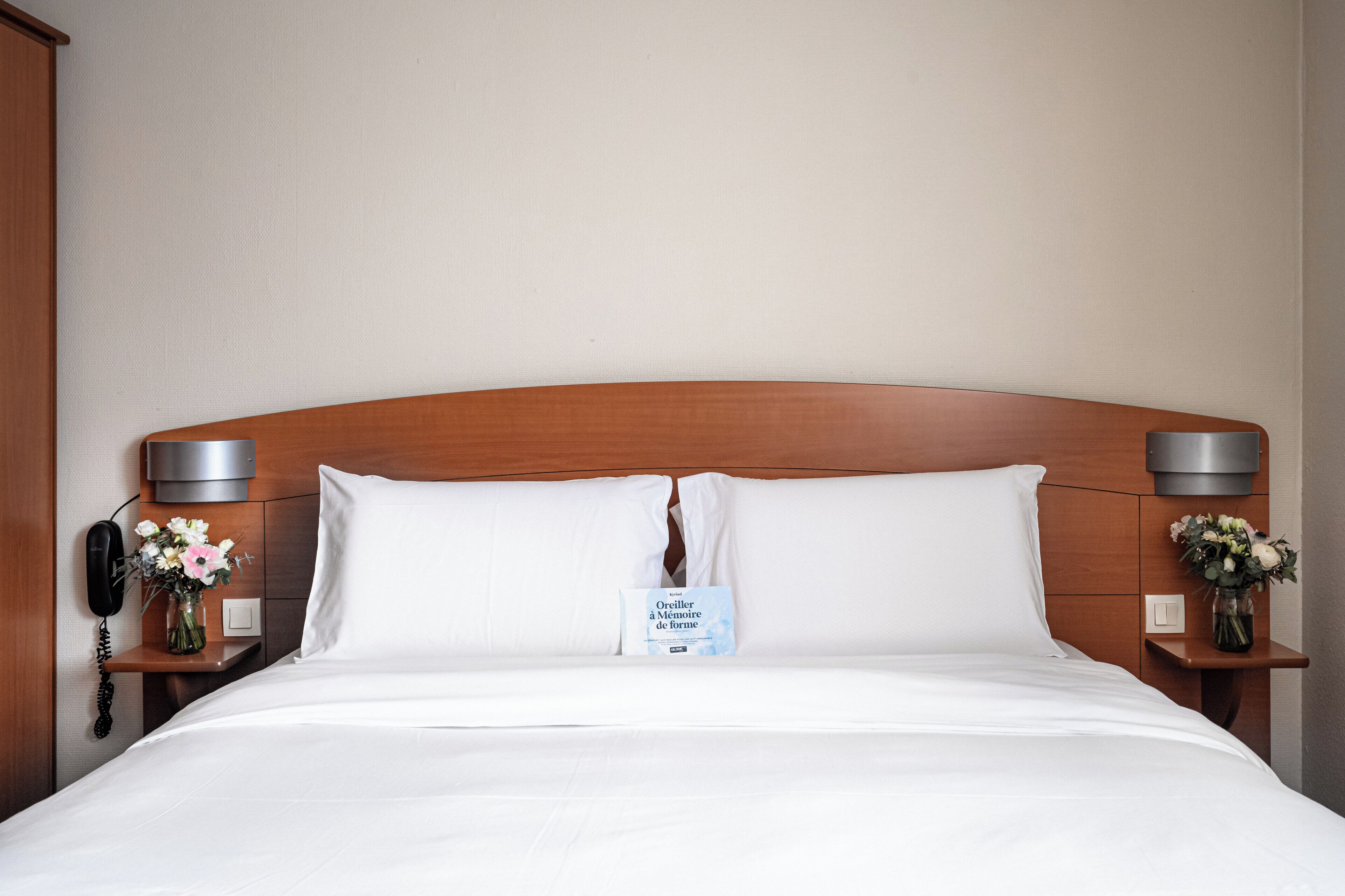 A neatly made bed with white linens, a wooden headboard, and two bedside tables with lamps and flower vases.