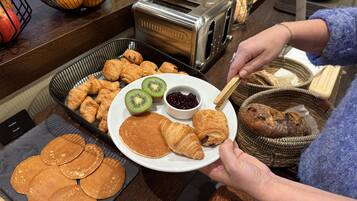 Buffet de café da manhã com pães, croissants e um prato com fatias de kiwi e geleia.