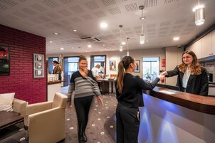 Un hall d’hôtel moderne comprenant un comptoir d’accueil, un espace salon et un mur décoratif en briques rouges.
