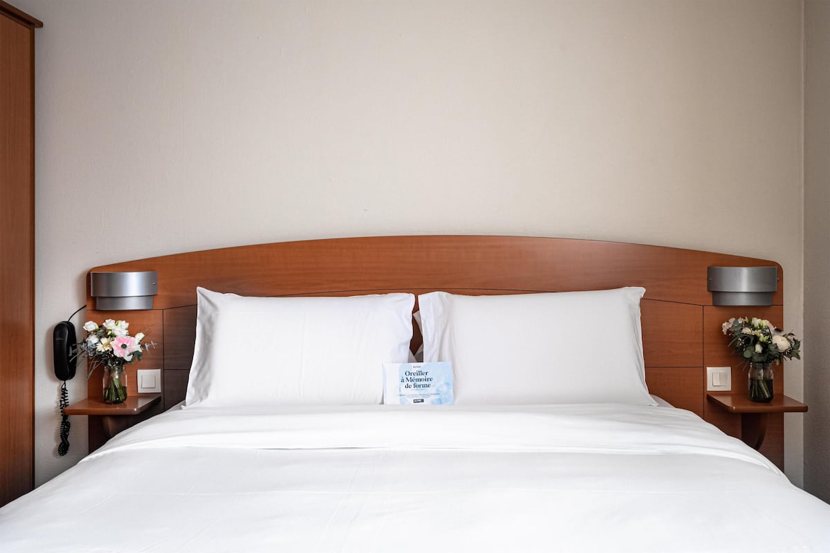 A neatly made bed with white linens, a wooden headboard, and two bedside tables with lamps and flower vases.