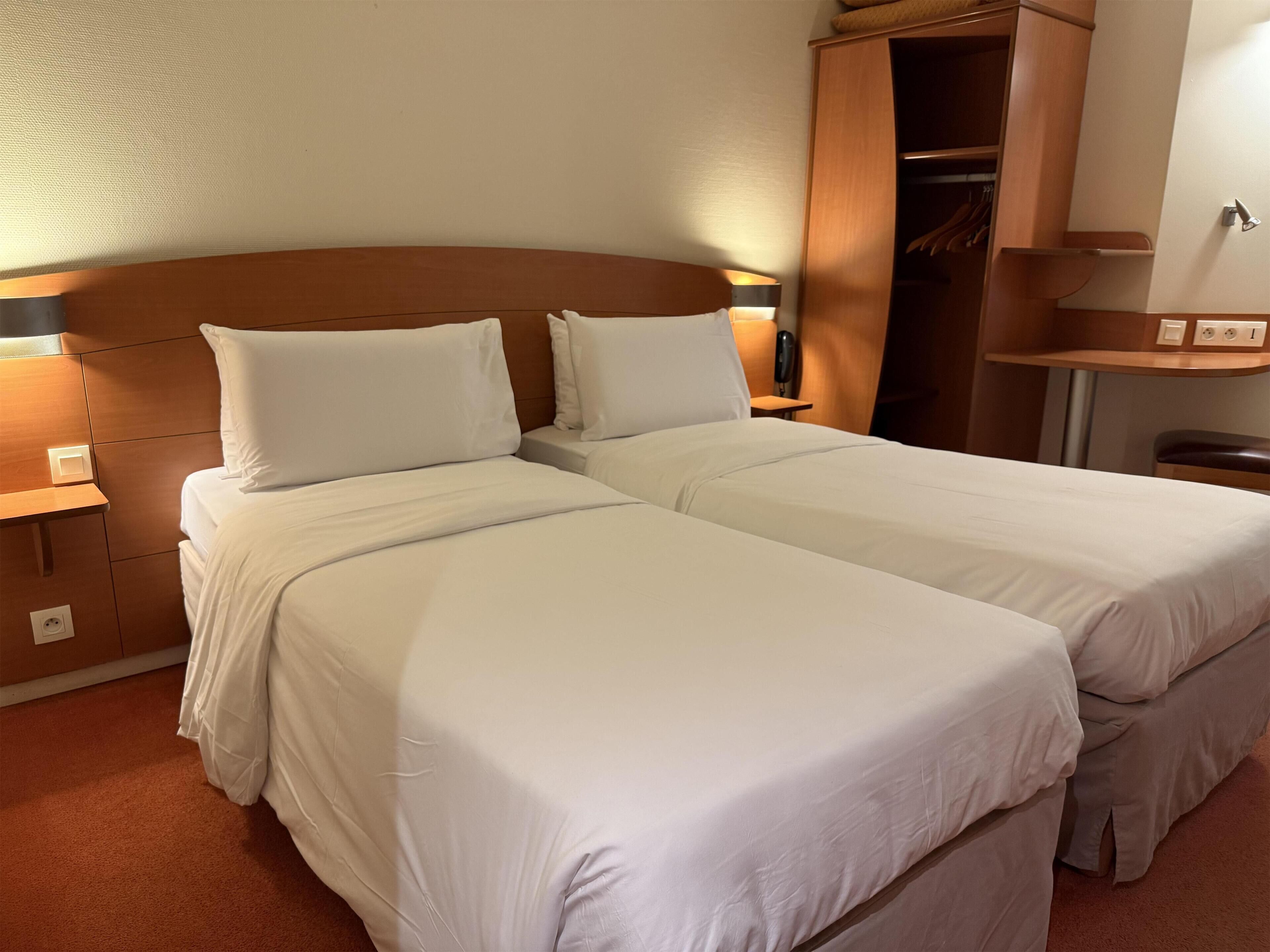 A double bed with white linens, a wooden headboard, and a nightstand with a lamp.