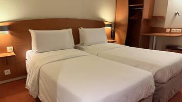 A double bed with white linens, a wooden headboard, and a nightstand with a lamp.