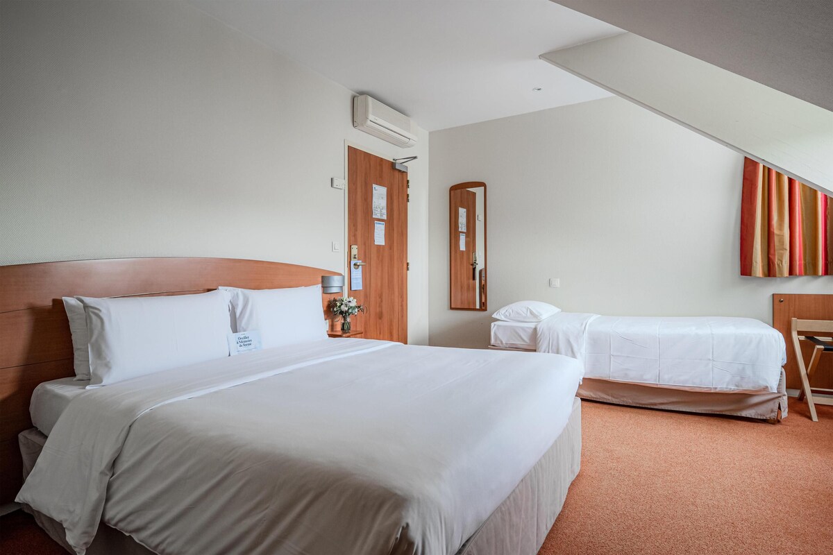 A hotel room with a large bed, a smaller bed, a wooden headboard, a mirror, and a door with a bulletin board.
