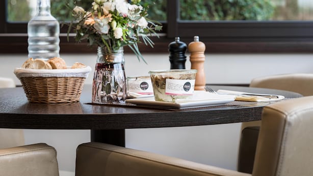 A dining table with a basket of bread, a jar of jam, a vase of flowers, and a plate of food. - Hôtel Kyriad Rennes Nord (Rennes)