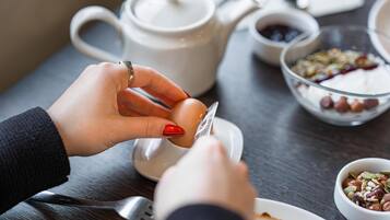 A person peeling an egg over a white plate, with a teapot and bowls of food in the background.