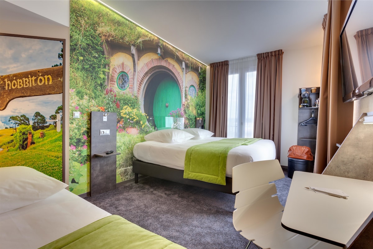 A hotel room with a bed, a desk, and a wall mural of a Hobbiton-style door.