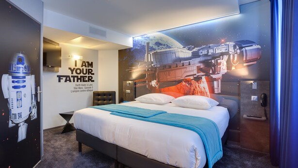 Un dormitorio con temática de Star Wars, con cama, almohadas, un mural en la pared y un cartel de R2-D2.