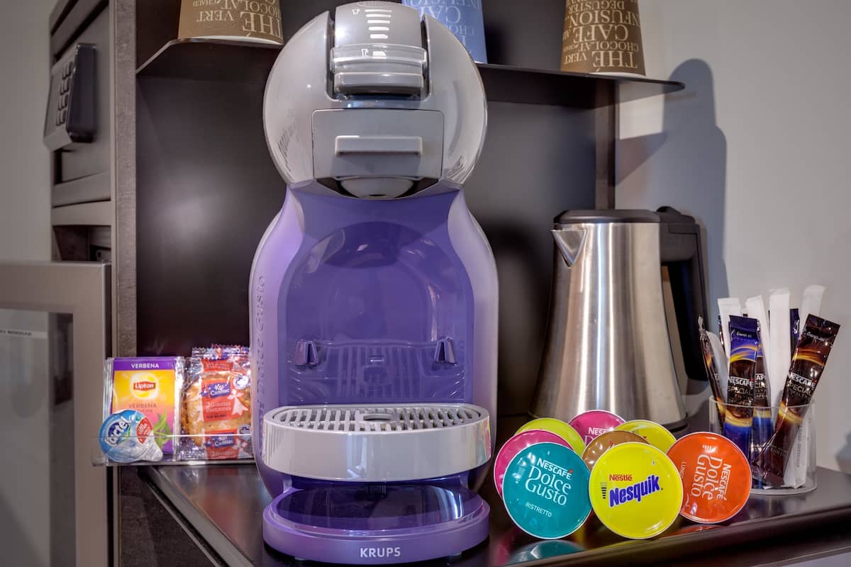A coffee machine with a purple and white design, a coffee pot, and various coffee pods and containers on a counter.