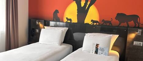 Habitación de hotel con dos camas individuales, un mural grande de un árbol y animales, y una mesita de noche con un teléfono.
