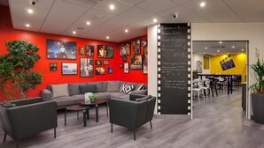 Una moderna zona de recepción con una pared roja, una pizarra con un mensaje de bienvenida y un área de estar con un sofá y sillones.
