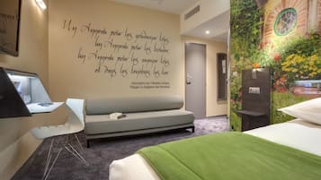 A modern hotel room with a sofa, a bed, a desk, and a unique wall mural.