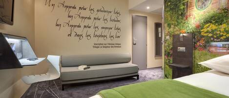 Una habitación de hotel moderna con sofá, cama, escritorio y un mural único en la pared.