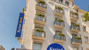 Un hotel con balcones, cielo despejado y un cartel que dice 'Kyriad Hotel'.