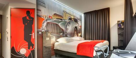 A modern hotel room with a bed, a desk, and a wall featuring a vintage car and a silhouette of a person.