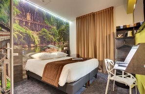 Habitación de hotel con cama, escritorio y un amplio ventanal con vistas panorámicas a un puente y un bosque.