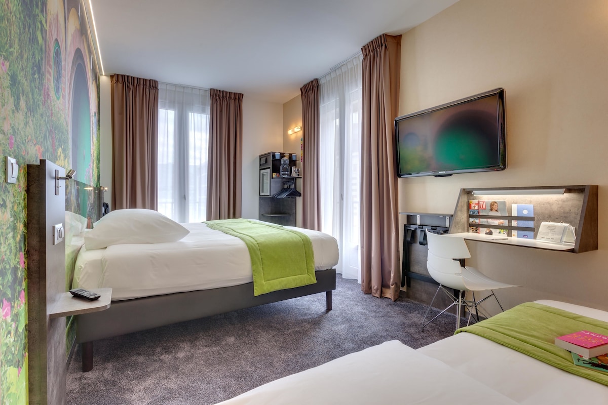 Habitación de hotel con cama, escritorio, silla, televisor y cafetera.