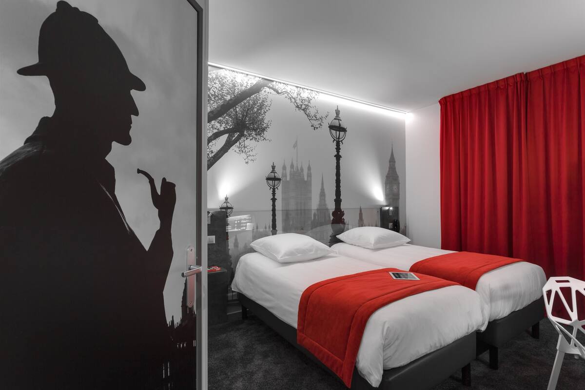 A hotel room with a large bed, two bedside tables, a red curtain, and a wall mural of a cityscape.